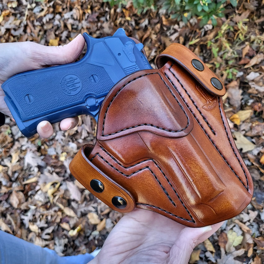 Georgia Snap 2 leather holster in vintage light brown for a Beretta 92 FS being held in hand over leaves.