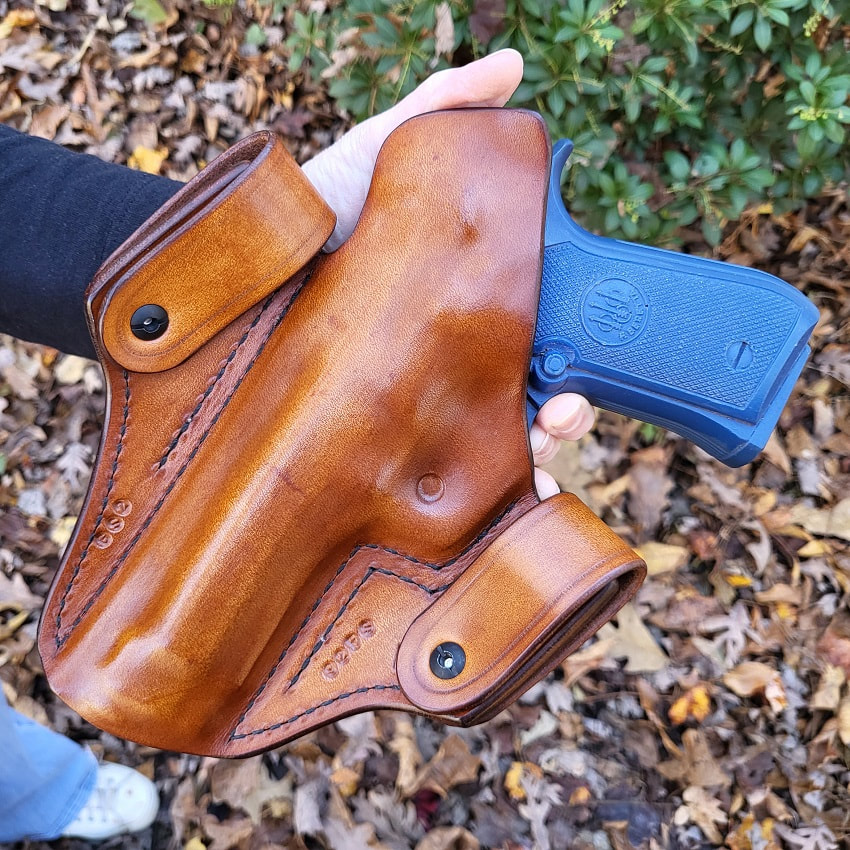 Back view of a Georgia Snap 2 leather holster in vintage light brown for a Beretta 92 FS being held in hand over leaves.